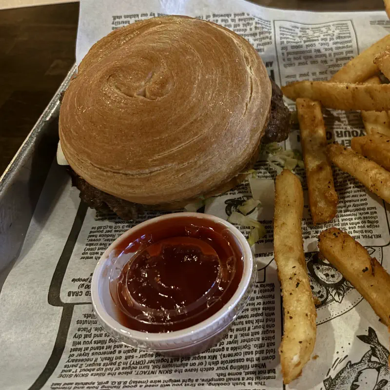 A smash burger with ketchup and seasoned fries on a paper-lined tray
