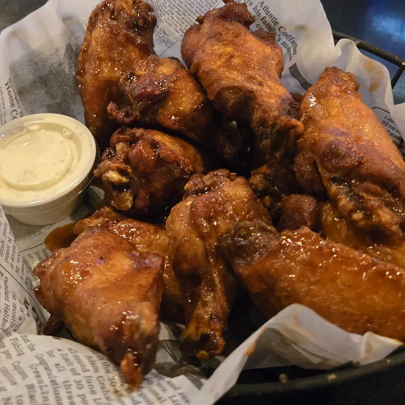 A basket of wings with a cup of dip, on newsprint